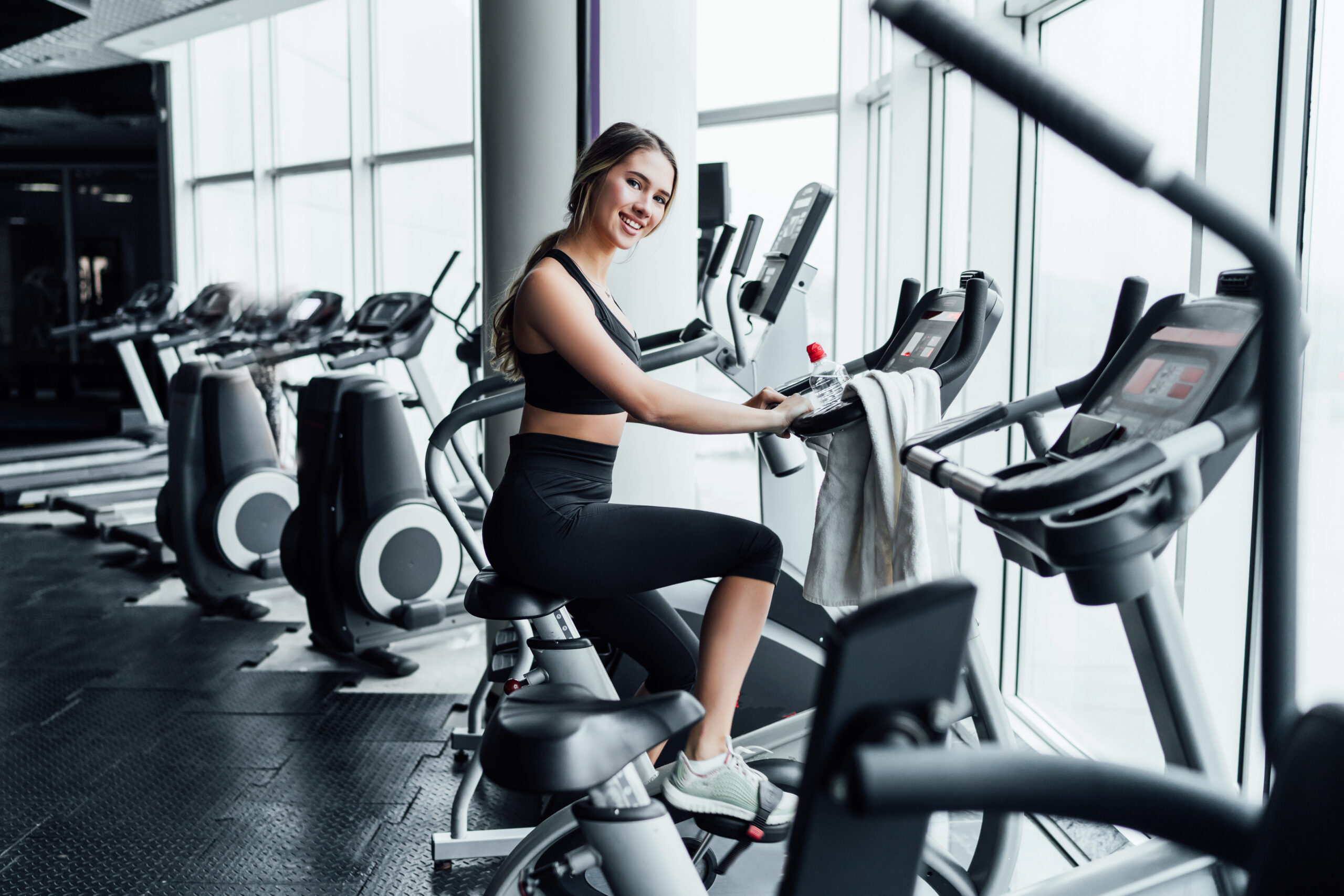 Attractive smiling girl on an exercise bike in a modern spacious gym, she is smiling at the camera, a healthy lifestyle.