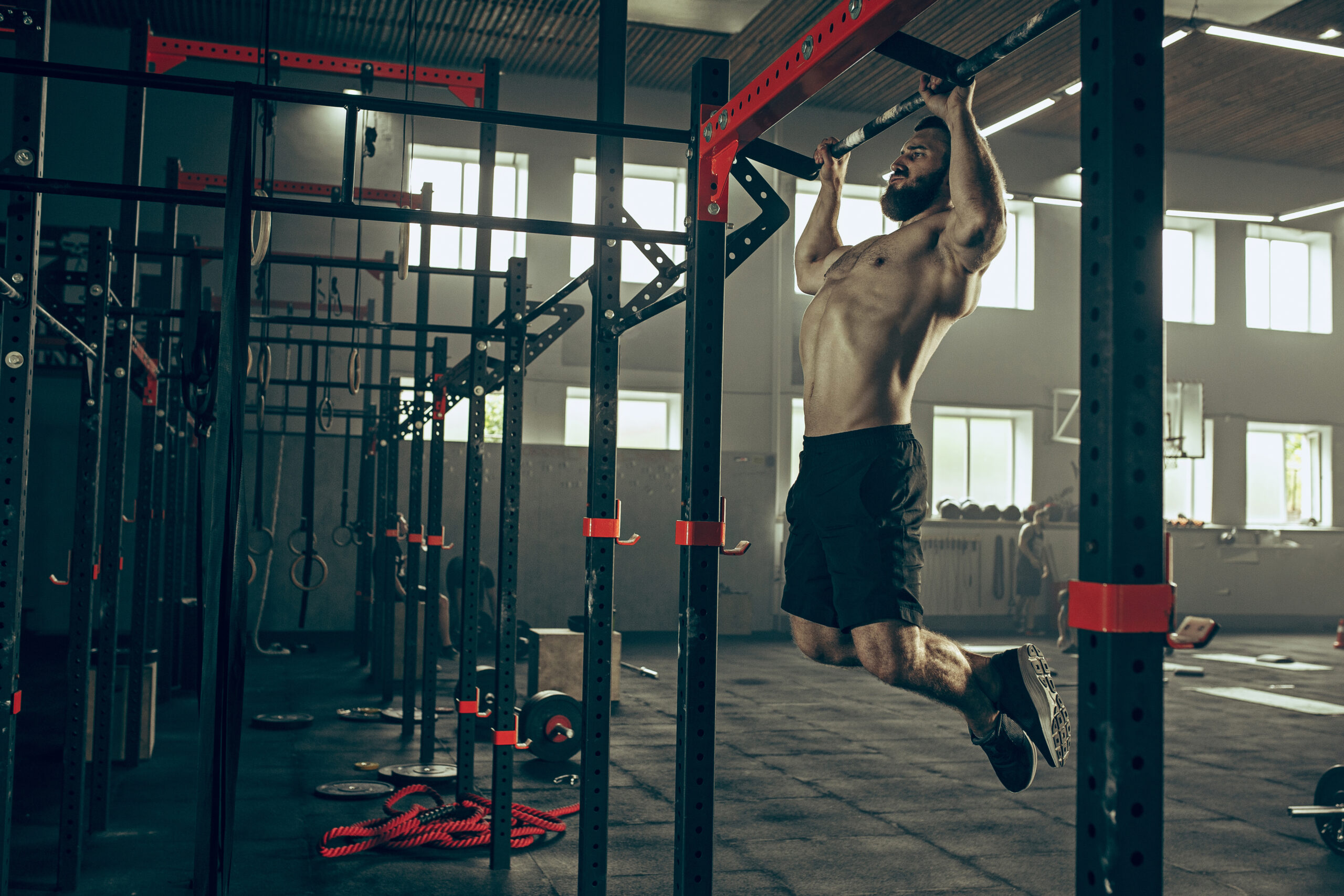 Concept: power, strength, healthy lifestyle, sport. Powerful attractive muscular man trainer do pull ups during workout at the gym